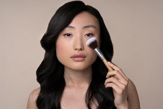 une femme asiatique applique du maquillage blush blanc